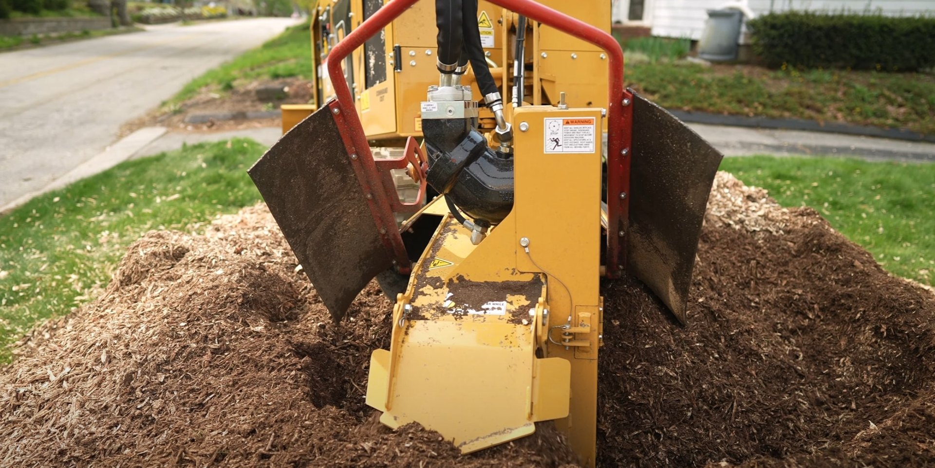 Residential stump removal creating wood mulch for landscaping Industrial stump grinder machine working on residential property with mulch piles